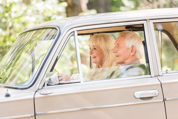 Zijaanzicht van senior man en vrouw beige auto rijden - Foto, afbeelding