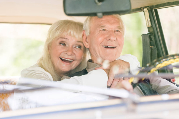 front view of beautiful excited senior woman hugging man in retro car - Foto, Imagen