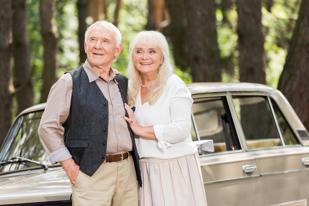 senior couple standing near retro car and looking away - Photo, Image