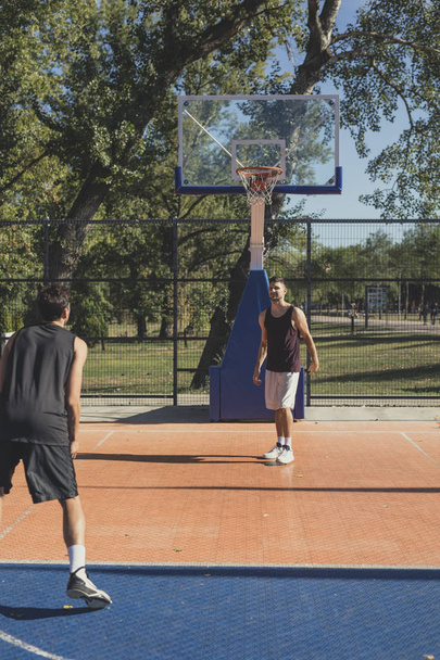 Young Caucasian man training basketball at outdoor court. - 写真・画像