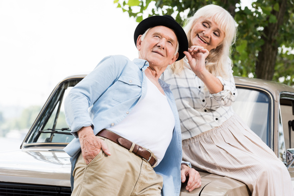 smiling senior man near woman sitting on beige retro car - Fotoğraf, Görsel