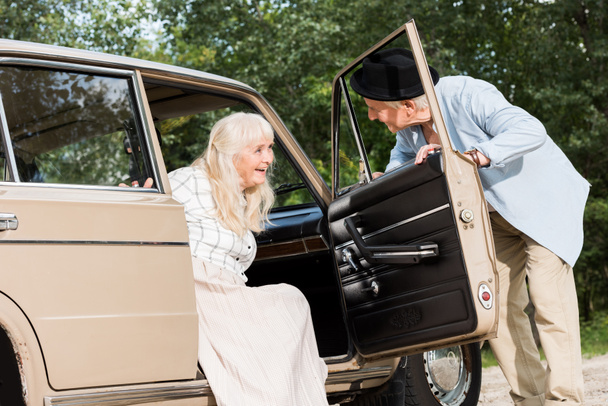 senior man opening car door in front of beautiful woman - Photo, Image