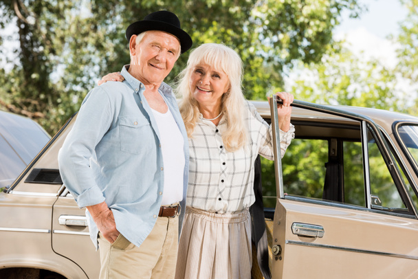 Senior man en vrouw staande in de buurt van retro auto en kijken naar camera  - Foto, afbeelding