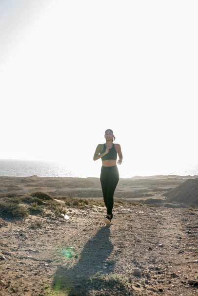 Жінка біжить коричневою піщаною дорогою в пустелі, з горами на задньому плані
 - Фото, зображення