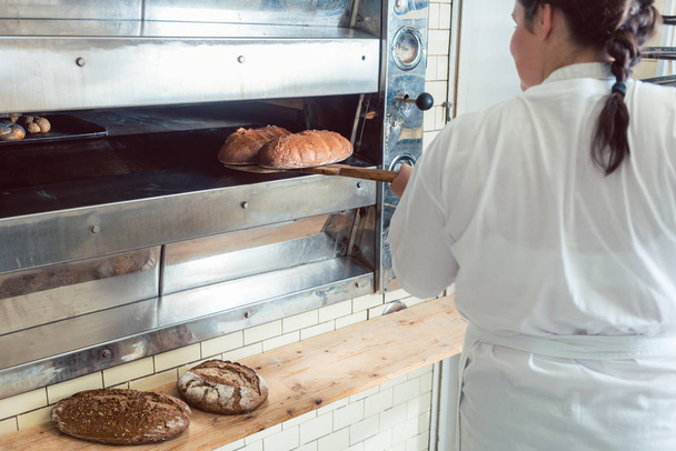 Baker getting fresh bread with shovel out of oven - Photo, Image