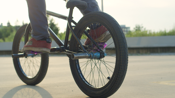 スローモーションをクローズ アップ: 認識できない極端な bmx バイク ペダルと美しい夏の日当たりの良い公園で自転車に乗って。クールな若い bmx バイク晴れた日に都市公園の日没の太陽の上のトリックを行う - 映像、動画