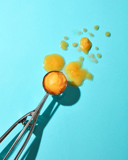  ball of yellow ice cream in metal spoon on blue background - Foto, afbeelding