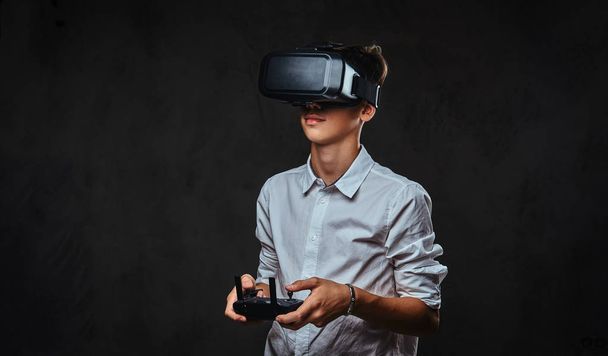 junger Teenager in weißem Hemd trägt Virtual-Reality-Brille und steuert den Quadrocopter mit der Fernbedienung. - Foto, Bild