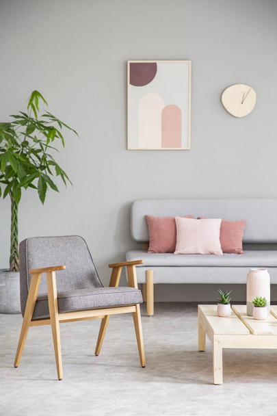 Poltrona de madeira cinza ao lado da mesa na sala de estar interior com cartaz acima do sofá. Foto real
 - Foto, Imagem