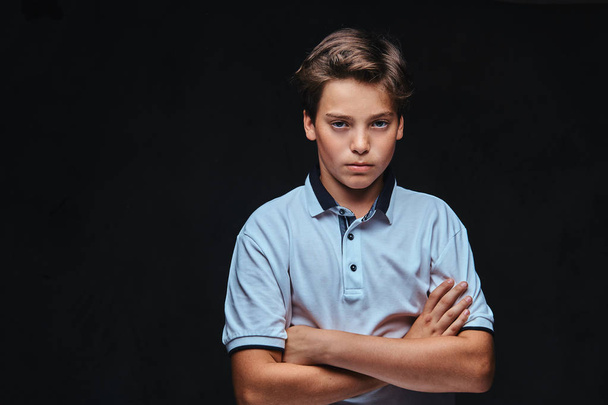Smutny kaukaski młody nastolatek ubrany w biały stojący t-shirt z skrzyżowanymi rękami. Na białym tle na ciemnym tle. - Zdjęcie, obraz