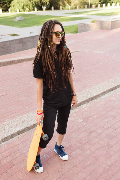 Stylish teenager holds a skateboard on a summer evening in the park - Foto, Imagem