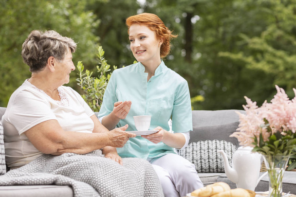 Ystävällinen hoitaja teetä puhumalla vanhempi nainen puutarhassa
 - Valokuva, kuva