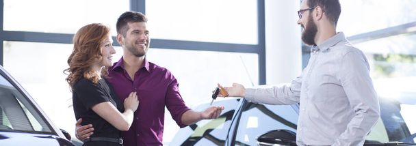 Panorama of professional car seller giving keys to smiling man and woman - Foto, afbeelding