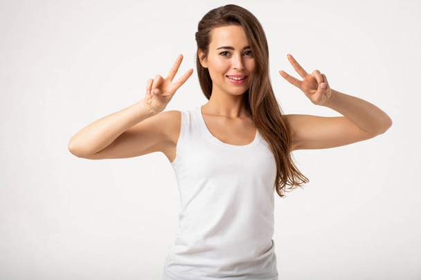 smiling brunette woman gesturing peace sign with hands standing on white background - Zdjęcie, obraz