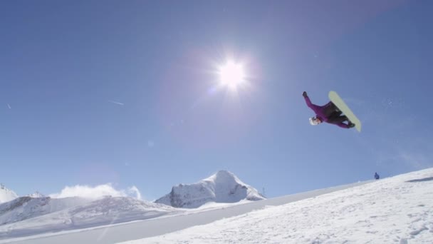Slow Motion: Mladí pro snowboardista na koni rampě v big mountain snow parku, skákání z halfpipe zdi a nad slunce, provádění triků a střídání s drapáky v slunných zimních - Záběry, video