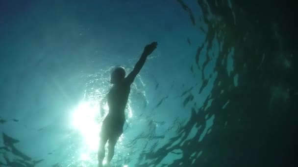 スローモーション、クローズ アップ、水中で低視野角: スポーティな若い男に水中での運動と形状に滞在するフロント クロールを泳ぐします。素晴らしい夏の日にガラスの海の表面を通して輝く太陽の光 - 映像、動画