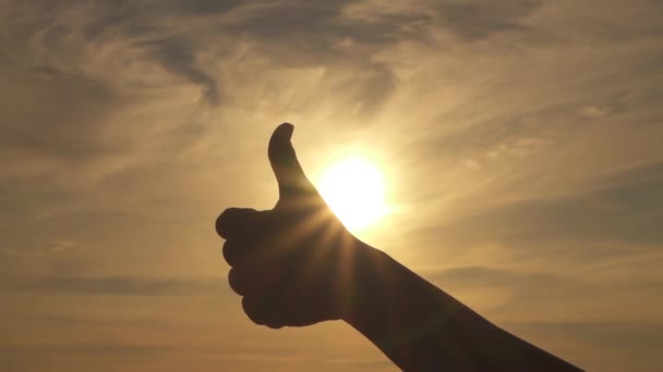SLOW MOTION, CLOSE UP: Putting extended thumb in the air from a closed fist. Giving thumbs up. Woman making nonverbal communication gestures, signs and symbols with stormy golden sky in background - Footage, Video