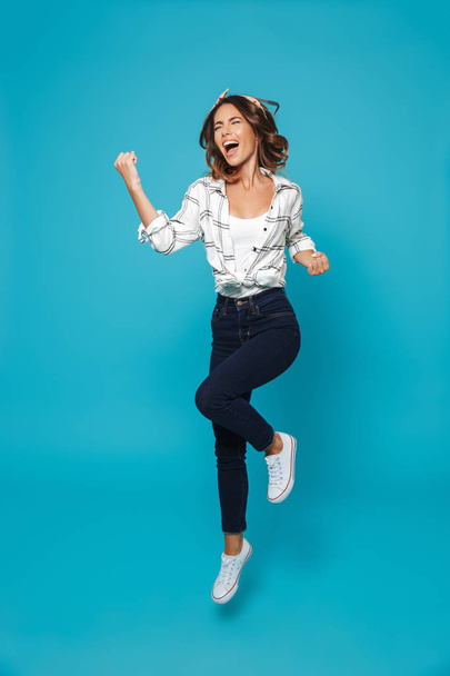 Full length portrait of a happy young housewife jumping isolated over blue background - Foto, immagini