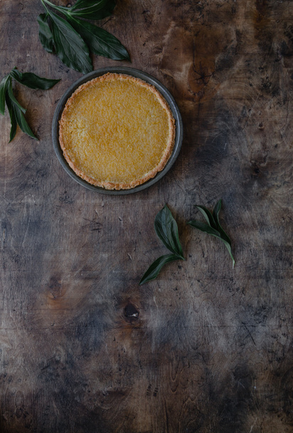top view of tasty lemon pie and leaves on wooden table - Foto, imagen