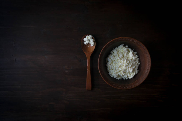 Cup of cottage cheese, wooden spoon on dark wooden background. The view from the top and copy space. - Foto, afbeelding