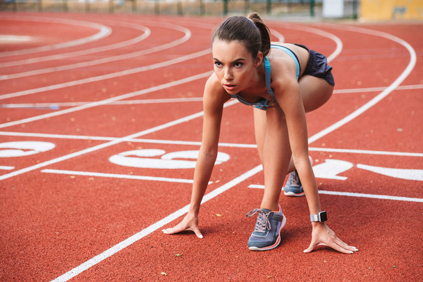 Confident young sportswoman getting ready to run a distance at the stadium - Foto, Imagem