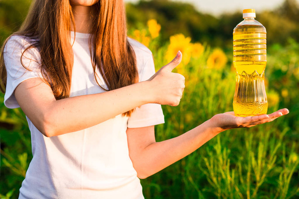 Mujer joven en botella blanca de aceite en el campo de girasol y mostrar los pulgares hacia arriba
 - Foto, Imagen