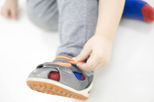 Small child tries to put on his shoes. Baby boy with shoes in hand. how to choose shoes for a child two years old. the problem of flat feet. - Fotó, kép