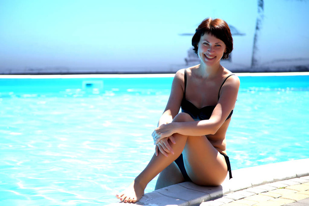 Beautiful mature woman posing for the camera against a turquoise water background. Woman in the pool. Beautiful sexy woman in pool during summer. - Valokuva, kuva