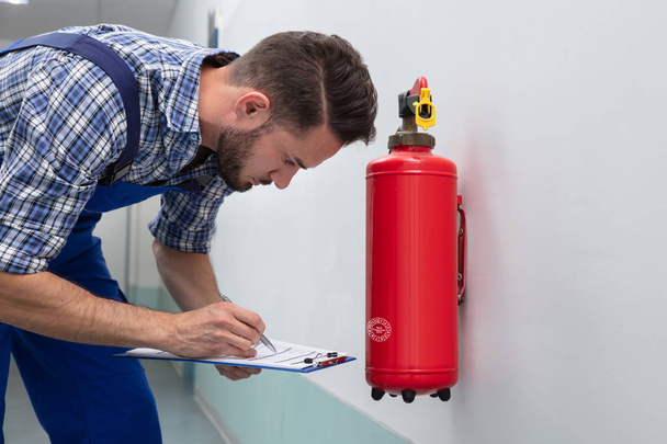 Young Male Technician Checking Symbol On Fire Extinguisher - Foto, imagen