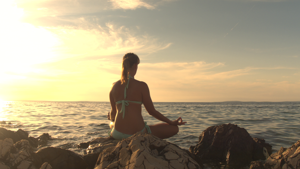 CLOSE UP: Молодая девушка, сидящая на скале у рябины моря, медитирующая в позе лотос-йоги, концентрирующаяся в тишине, наблюдающая дыхание, расслабляющая ум, душу и тело. Спокойная женщина пытается достичь гармонии дзен
 - Кадры, видео