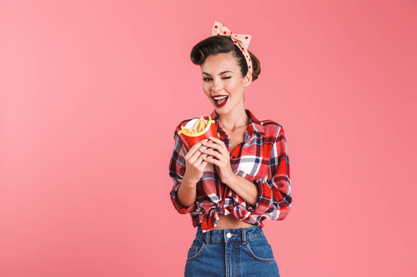 Picture of happy young pin-up woman isolated over pink background wall holding french fries. - Fotografie, Obrázek