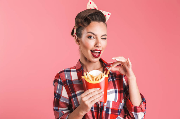 Picture of happy young pin-up woman isolated over pink background wall holding french fries. - Fotó, kép