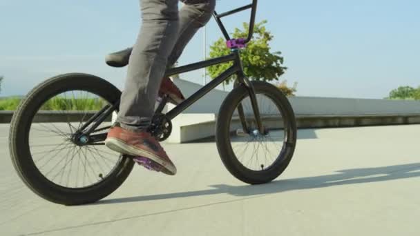 Zeitlupe aus nächster Nähe: Extrembiker treten in die Pedale und springen im Sommer im sonnigen Park Hasenhüttl-Tricks. cooler junger BMX-Biker bei Ollie-Tricks und 360-Grad-Drehung im Stadtpark an sonnigem Tag - Filmmaterial, Video