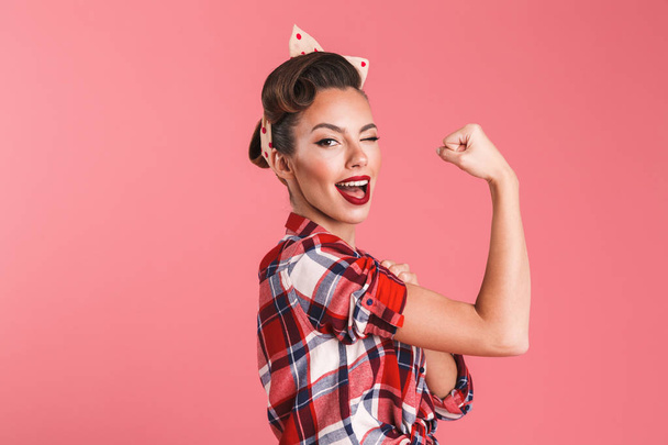 Photo of gorgeous strong young pin-up woman isolated over pink background wall showing biceps winking. - 写真・画像