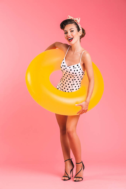 Photo of happy young pin-up woman isolated over pink background wall in swimwear with inflatable ring. - Fotó, kép