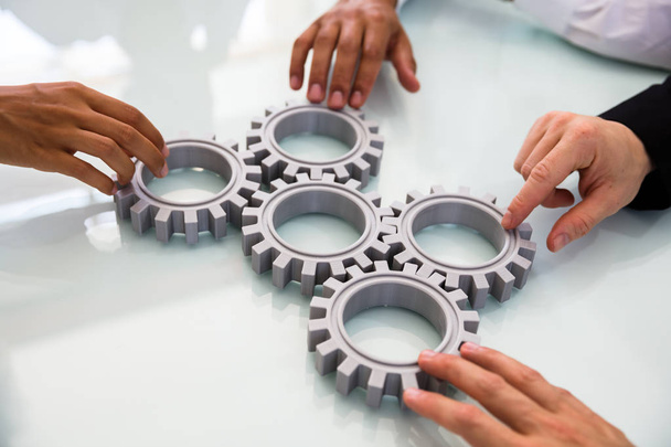 Close-up Of Business People's Hand Connecting Gears On Desk - 写真・画像