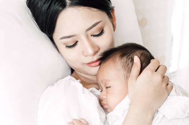 Μητέρα εκμετάλλευση μωρό στην αγκαλιά και φιλί σε μια λευκή κρεβατοκάμαρα. Η αγάπη της οικογένειας έννοια - Φωτογραφία, εικόνα
