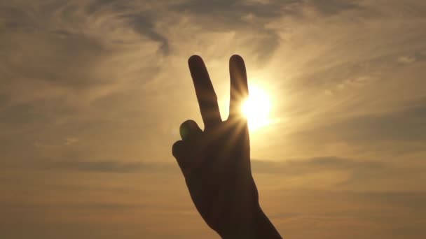SLOW MOTION CLOSE UP DOF: Showing a victory hand gesture, raising and parting index and middle fingers, while the other fingers are clenched. Peace sign with sunny stormy cloudy sky and in background - Footage, Video