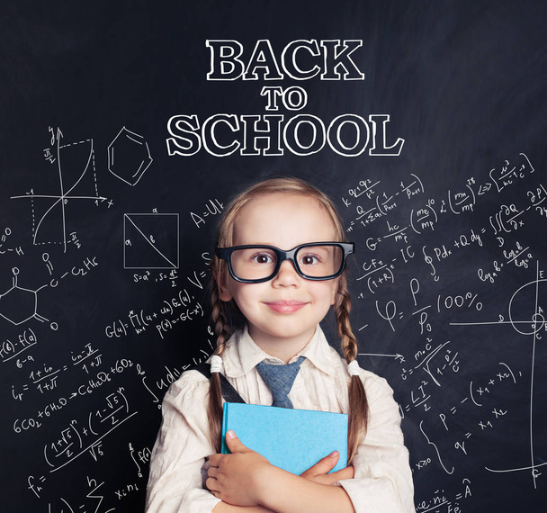 glückliches Kind lächelnd und mit blauem Buch auf Tafel-Hintergrund mit naturwissenschaftlichem Kreidemuster. zurück zum Schulkonzept - Foto, Bild