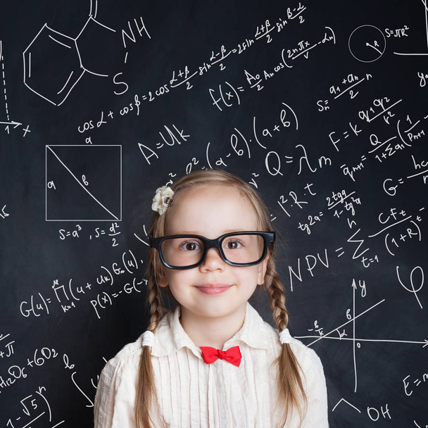 Little genius. Smart little girl math student on school blackboard background with hand drawings science formula pattern. Kids mathematics education concept - Photo, image