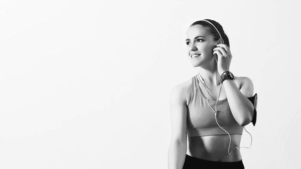 Young sporty woman listening to music with earphones on smart phone app for fitness motivation. Beautiful girl in sportswear relaxing and looking aside indoor. Weight Loss. Healthy lifestyle - Foto, Imagen