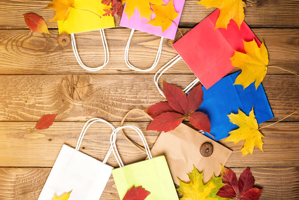 Color shopping paper bags and autumn leaves, flat lay, copy space. Autumn shopping, sales concept. Autumn holiday. Shopping in autumn - Photo, image