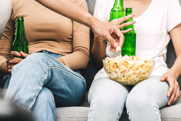 Group of friends eating popcorn and drinking beer together on sofa at home.Friendship and party  concept - Photo, Image