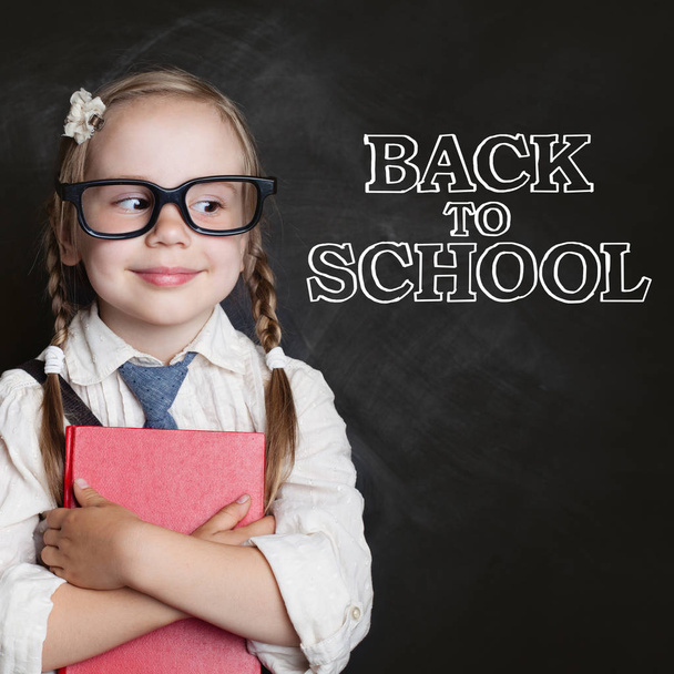 Little girl student with red book on chalk board background, back to school concept - Photo, Image