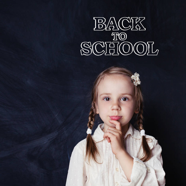 kleines Mädchen, das im Klassenzimmer auf Tafel-Hintergrund mit der Schulhandschrift denkt. Chancen und zurück zum Schulkonzept - Foto, Bild