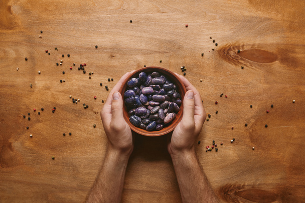Male hands holding bowl filled with haricot beans on wooden table - Foto, immagini