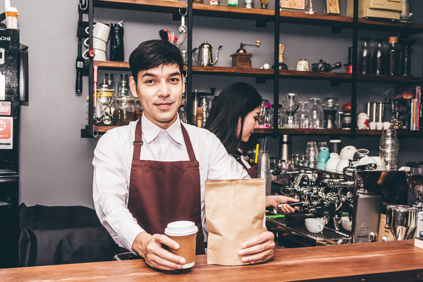 Handsome barista standing behind a counter and giving coffee cup to customer at cafe - Photo, Image