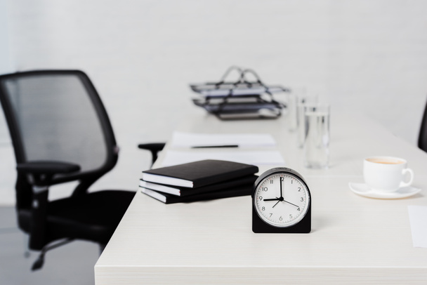 primer plano de escritorio con pila de cuadernos y reloj despertador en la oficina moderna
 - Foto, Imagen