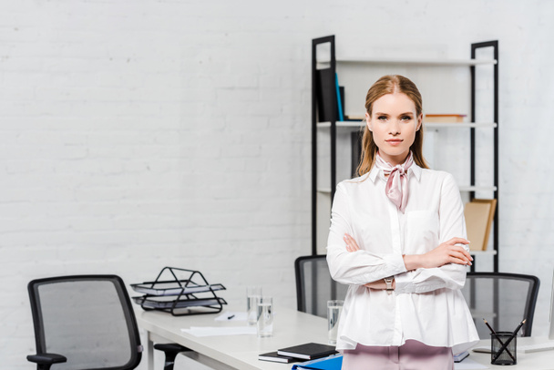 beautiful young businesswoman with crossed arms looking at camera at modern office - Foto, afbeelding