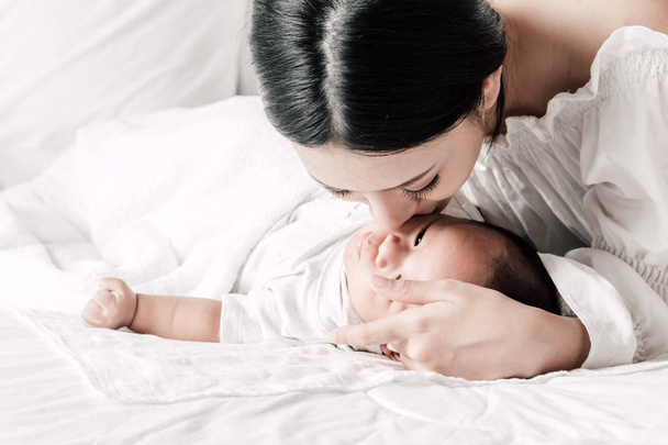 Äiti pitää vauvaa sylissään ja suudella valkoisessa makuuhuoneessa.Rakkaus perheen käsite
 - Valokuva, kuva